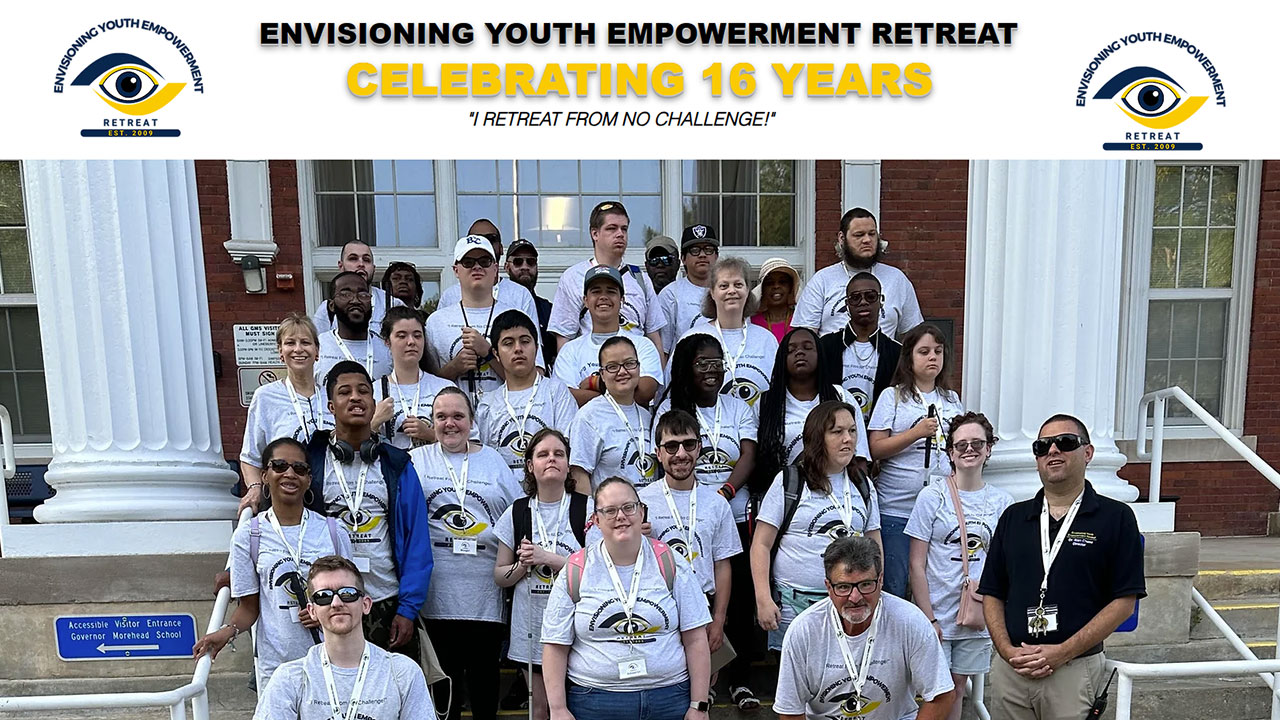 A diverse group of approximately thirty people, including both adults and teenagers, pose for a group photo on the steps of a brick building with large white columns. They are participants of the Envisioning Youth Empowerment Retreat, celebrating its 16th year. Most of the group members wear matching white T-shirts featuring the retreat's logo, which includes an eye graphic and the words 'Envisioning Youth Empowerment Retreat.' Some people are wearing sunglasses, while others have lanyards and name badges. The background includes a blue sign reading 'Accessible Visitor Entrance Governor Morehead School.' The event banner above the group highlights the celebration with the text: 'ENVISIONING YOUTH EMPOWERMENT RETREAT CELEBRATING 16 YEARS 'I RETREAT FROM NO CHALLENGE!'